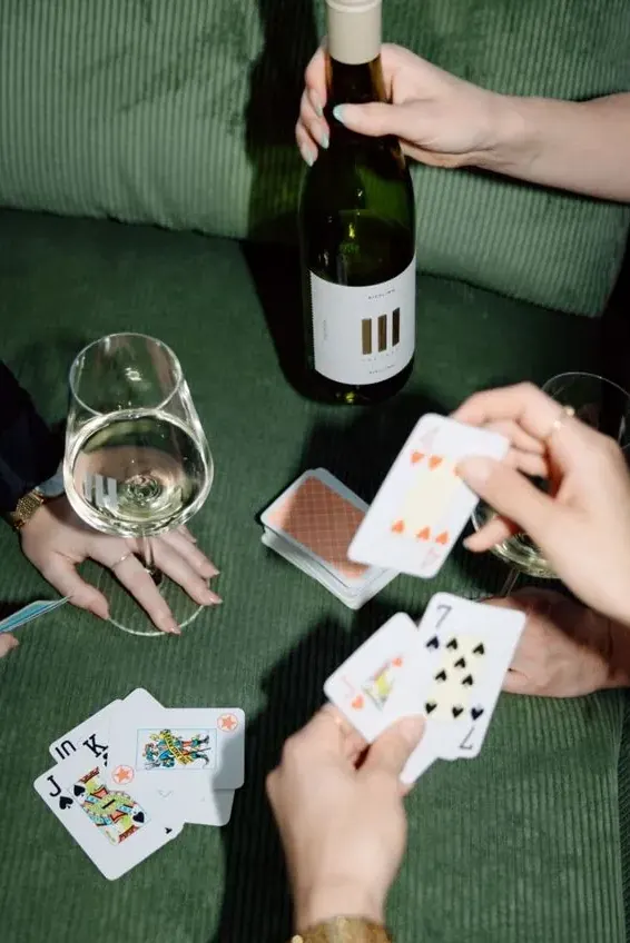 Friends playing cards around a bottle of white wine