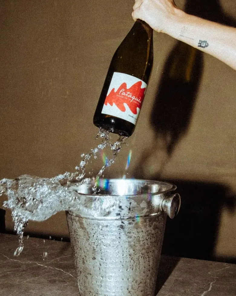 A bottle of natural wine poured into a splashing ice bucket