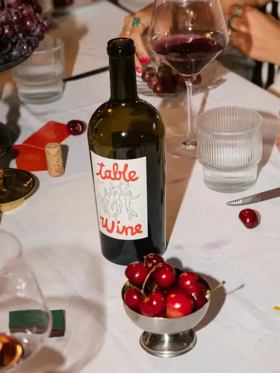 A bottle of red Table Wine on a dinner table with cherries and glasses