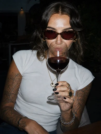 A woman in sunglasses sipping a glass of red wine